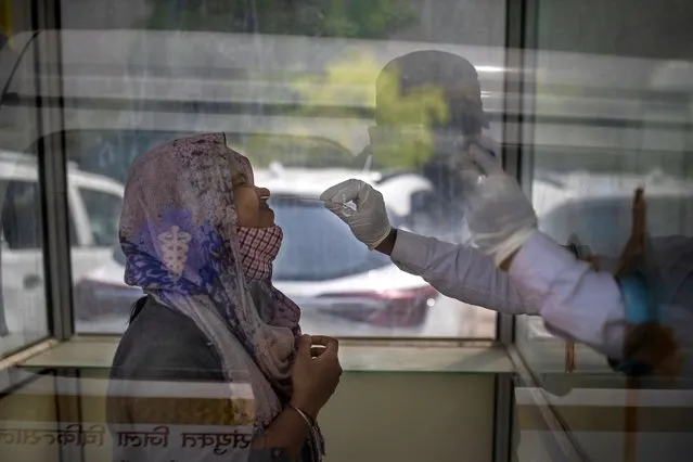 A health worker takes a swab sample to test for COVID-19 at a government hospital in Noida, a suburb of New Delhi, India, Wednesday, April 7, 2021. India hits another new peak with 115,736 coronavirus cases reported in the past 24 hours with New Delhi, Mumbai and dozens of other cities imposing night curfews to check the soaring infections. (Photo by Altaf Qadri/AP Photo)