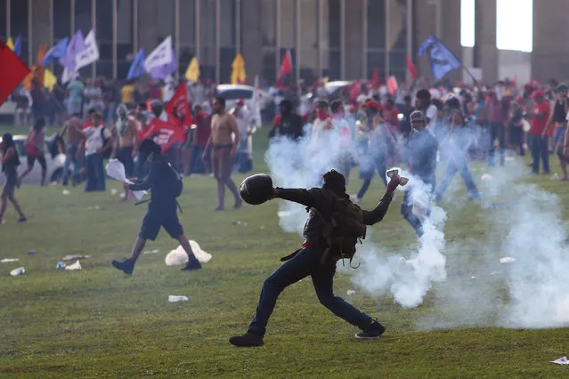 An anti-government demonstrator throws back a tear gas canister during a clash with riot policemen during a protest against a constitutional amendment, known as PEC 55, that limits public spending, in front of Brazil's National Congress in Brasilia, Brazil November 29, 2016. (Photo by Adriano Machado/Reuters)