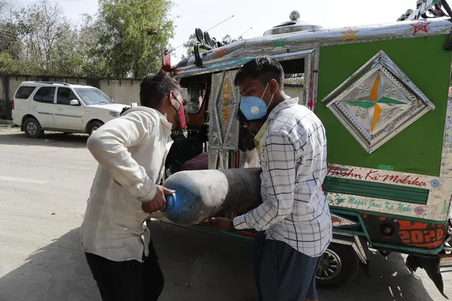 People carry a medical oxygen cylinder at a charging station on the outskirts of Prayagraj, India, Friday, April 23, 2021. India put oxygen tankers on special express trains as major hospitals in New Delhi on Friday begged on social media for more supplies to save COVID-19 patients who are struggling to breathe. India's underfunded health system is tattering as the world's worst coronavirus surge wears out the nation, which set another global record in daily infections for a second straight day with 332,730. (Photo by Rajesh Kumar Singh/AP Photo)