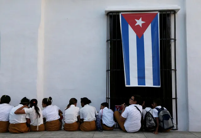 School children sit on a sidewalk while waiting for the ashes of Cuba's former President Fidel Castro to pass during a journey to the eastern city of Santiago de Cuba, in Bayamo, Cuba, December 2, 2016. (Photo by Edgard Garrido/Reuters)