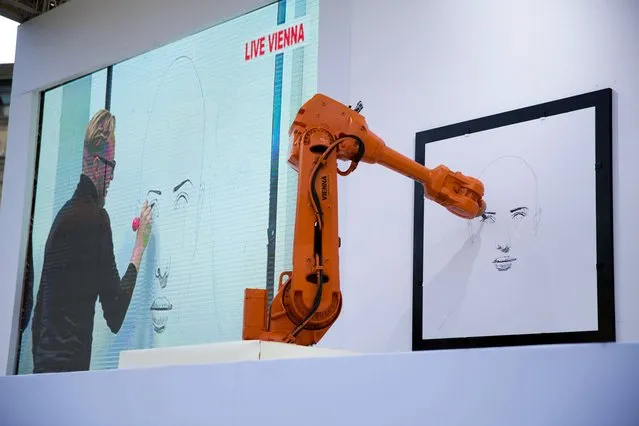 Austrian artist Alex Kiessling is shown working on a drawing live from Vienna on a big screen in Trafalgar Square, London, as robot arms in London, right, and Berlin replicate his work, Thursday, September 26, 2013.  The project has been given the title “Long Distance Art” and utilizes the IRB 4600 robotic arms, produced by the company ABB for industrial manufacturing in areas such as automotive, plastics, metal fabrication and electronics. (Photo by Matt Dunham/AP Photo)