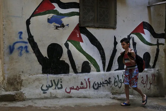 In this Thursday, May 4, 2017 photo, a boy walks by graffiti of the Palestinian flags with Arabic reads: “The flag is four colors that shine on the face of the sun” in the Bourj al-Barajneh Palestinian refugee camp in Beirut, Lebanon. (Photo by Bilal Hussein/AP Photo)