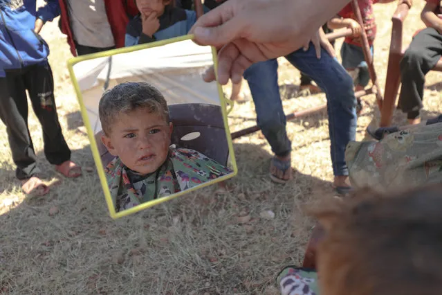 Syrian child looks his hairstyle in a hand mirror as volunteer barbers give free haircuts to children who escaped from the attacks of the Assad regime and settled in makeshift tents, ahead of the upcoming Eid al-Fitr in Idlib, Syria on May 12, 2021. (Photo by Izzettin Kasim/Anadolu Agency via Getty Images)