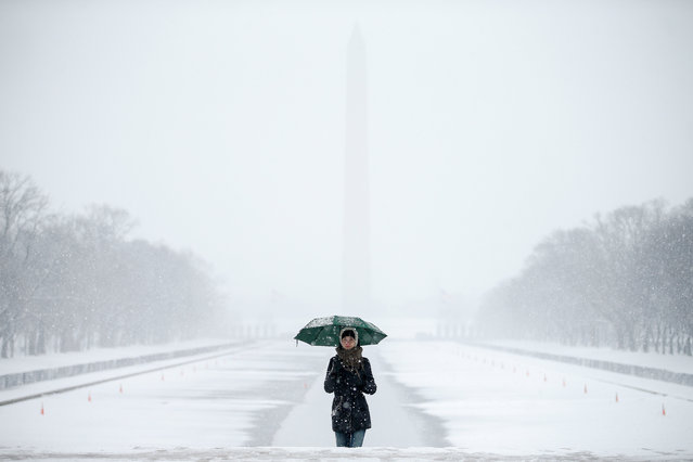 The Washington Monument and the Reflecting Pool are visible behind Claudia Marusanici, visiting from Romania, as she makes her way towards the Lincoln Memorial on the National Mall in Thursday, March 5, 2015, in the falling snow.  (AP Photo/Andrew Harnik)