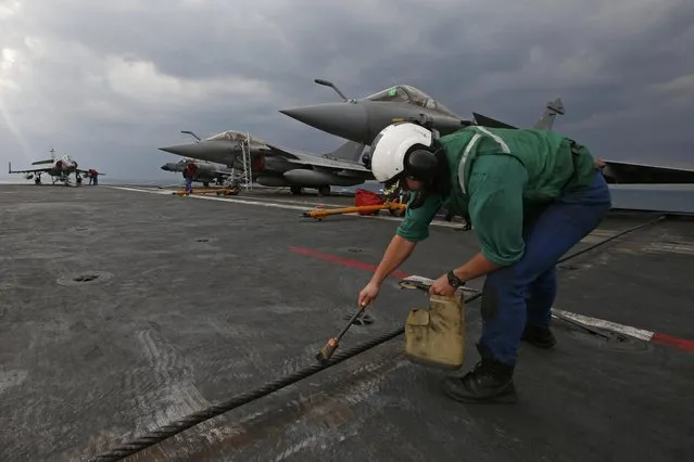 A crew member greases one of the three arresting cables used to stop fighter jets when they land on the flight deck aboard France's Charles de Gaulle aircraft carrier in the Gulf, January 29, 2016. (Photo by Philippe Wojazer/Reuters)