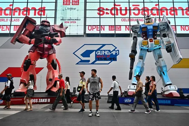 A man poses for a picture in between two giant Gundam statues by Bandai Namco in front of Central World shopping mall in Bangkok on October 16, 2023. (Photo by Lillian Suwanrumpha/AFP Photo)