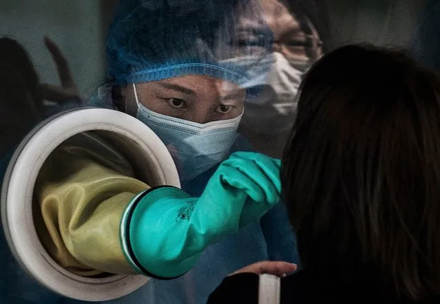 A medical worker wears protective clothing while performing a nucleic acid test on a client from behind glass at a small private testing site on August 6, 2021 in Beijing, China. While cases still remain relatively low compared to many countries, China is battling its worst COVID-19 outbreak in months after workers in the arrivals area at Nanjing International Airport were infected with the highly contagious Delta variant and it has since spread to dozens of cities in at least 18 provinces. (Photo by Kevin Frayer/Getty Images)