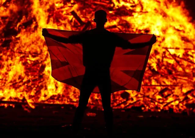 A person holds a flag in front of the Loyalist Corcrain Redmanville bonfire, which was lit to mark the start of the unionist Twelfth celebrations, in Portadown, Northern Ireland, July 11, 2021. (Photo by Jason Cairnduff/Reuters)