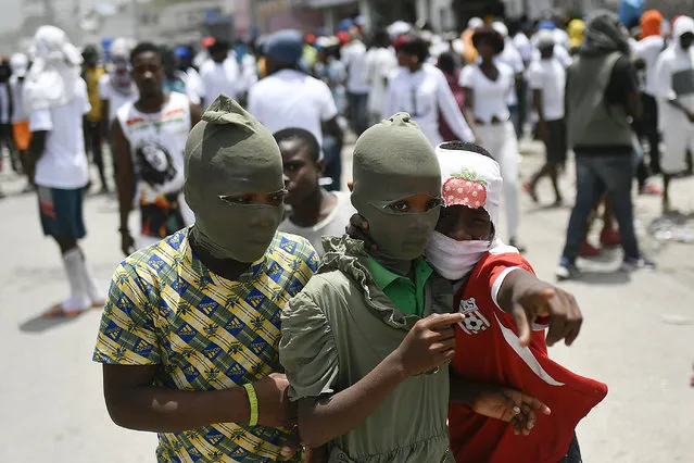 Children with their faces covered, join a march led by Jimmy Cherizier, alias Barbecue, a former police officer who heads a gang coalition known as “G9 Family and Allies”, to demand justice for slain Haitian President Jovenel Moise in La Saline neighborhood of Port-au-Prince, Haiti, Monday, July 26, 2021. (Photo by Matias Delacroix/AP Photo)