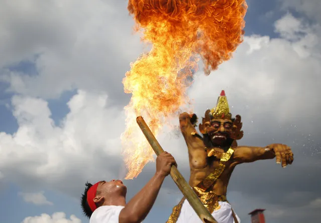 A Balinese Hindu blows fire, during a parade carrying Ogoh-ogoh effigies symbolising evil spirits, during a ritual before Nyepi, the day of silence, in Palembang, South Sumatra province, Indonesia March 8, 2016. Nyepi is a day of silence for self-reflection celebrating the Balinese Hindu new year, where people may not use lights, light fires, work, travel nor enjoy entertainment. (Photo by Darren Whiteside/Reuters)