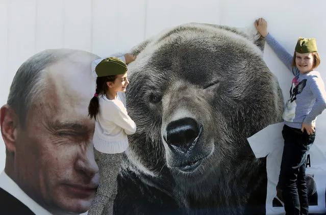 Russian children in field caps play near a poster showing Vladimir Putin and a bear at the Victory park in Moscow, Russia, 08 May 2015.  On May 09 Russia will celebrate the 70th anniversary of the victory of the Soviet Union and it's Allies over Nazi Germany in WWII. (Photo by Anatoly Maltsev/EPA)