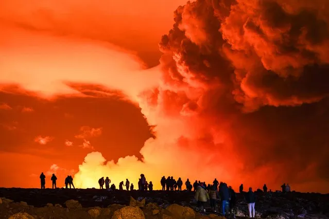 People gather to watch as molten lava flows out from a fissure on the Reykjanes peninsula north of the evacuated town of Grindavik, western Iceland on March 16, 2024. Lava spewed Saturday from a new volcanic fissure on Iceland's Reykjanes peninsula, the fourth eruption to hit the area since December, authorities said. (Photo by Ael Kermarec/AFP Photo)