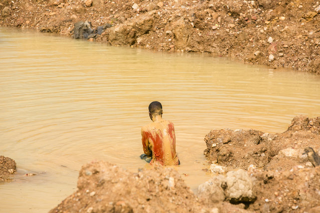 A mud-stained worker crouches in the water as he sifts for gold in Ghana, West Africa, 2014. (Photo by Heidi Woodman/Barcroft Images)
