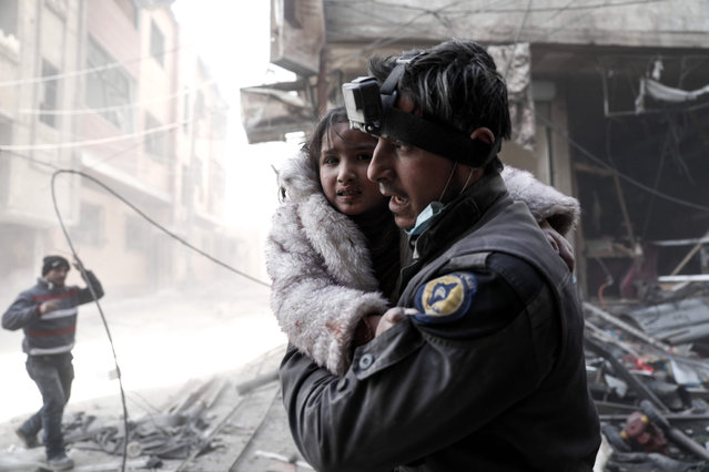 A member of the Syrian Civil Defence volunteers, also known as the White Helmets, carries a wounded girl amid the rubble following reported government airstrike on the rebel- held town of Douma, on the eastern outskirts of the capital Damascus, on February 25, 2017. Syrian regime forces carried out raids on several areas in the country, targeting mainly the besieged town of Douma, causing the deaths of at least 13 civilians, according to Syrian Observatory for Human Rights. (Photo by Sameer Al-Doumy/AFP Photo)