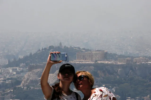 Tourists take photos as the Parthenon temple sits atop the Acropolis hill amidst thick smoke from a wildfire burning at the island of Evia some 70 km north of Athens, Greece, 13 August 2019. (Photo by Kostas Tsironis/EPA/EFE)