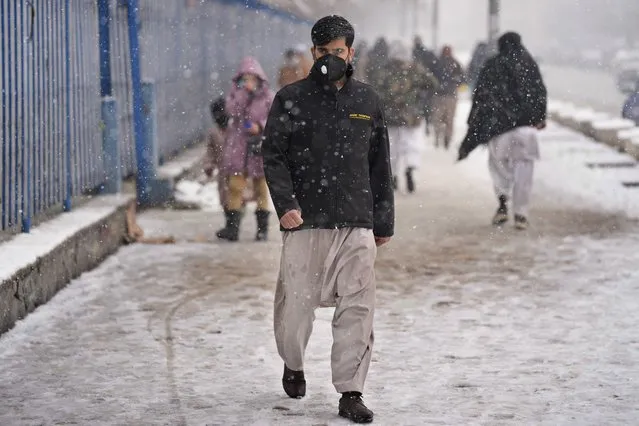 An Afghan man wears a mask to help curb the spread of COVID-19, as he walks in the snow, in Kabul, Afghanistan, Sunday, February 6, 2022. (Photo by Hussein Malla/AP Photo)
