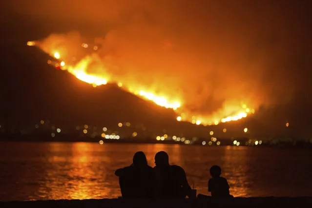 In this August 9, 2018, file photo, a family sits along the shore of Lake Elsinore as they watch the Holy Fire burn in the distance in Lake Elsinore, Calif. The National Interagency Fire Center is predicting a heavy wildfire season for areas along the west coast of the United States this summer. The Boise, Idaho-based center said Wednesday, May 1, 2019, that most of the country can expect a normal wildfire season in the period from May through August. (Photo by Patrick Record/AP Photo/File)