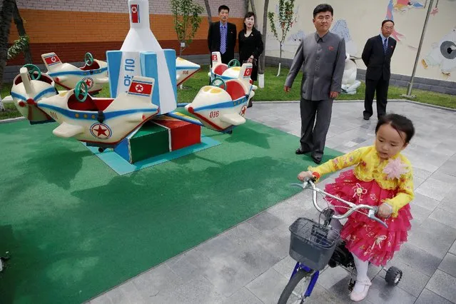 A girl rides a bicycle past a rocked shaped merry-go-around as official guides accompanying foreign reporters stand behind at the kindergarten of the Kim Jong Suk Pyongyang textile mill during a government organised visit for reporters in Pyongyang, North Korea May 9, 2016. (Photo by Damir Sagolj/Reuters)