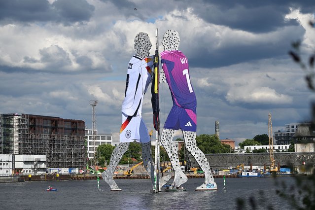 The “Molecule Man' sculpture designed by US artist Jonathan Borofsky is pictured wearing the three different Germany's national kits in the water of the river Spree in Berlin on June 13, 2024, ahead of the UEFA Euro 2024 European Football Championship. (Photo by Ralf Hirschberger/AFP Photo)