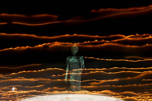 People walk with candle lights around a large Buddha statue during a ceremony commemorating Asalha Puja Day, an annual celebration marking the beginning of Triple Gem at a temple in Nakhon Pathom province on the outskirts of Bangkok, Thailand, on July 20, 2024. (Photo by Chalinee Thirasupa/Reuters)