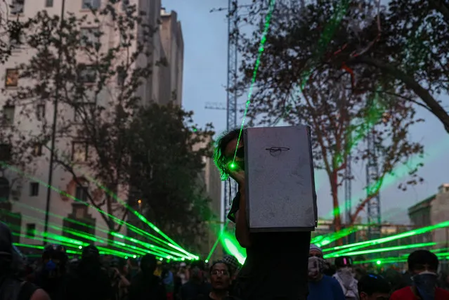 Anti-government demonstrators shine laser pointers a the police during a protest in Santiago, Chile, Thursday, November 14, 2019. Students in Chile began protesting nearly a month ago over a subway fare hike. The demonstrations have morphed into a massive protest movement demanding improvements in basic services and benefits, including pensions, health, and education. (Photo by Esteban Felix/AP Photo)