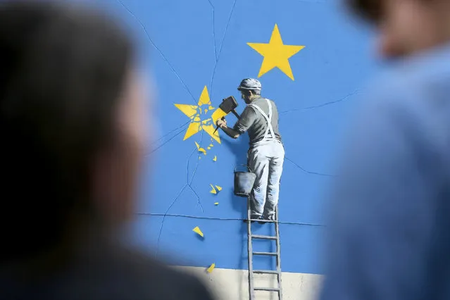 People stand near a recently painted mural by British graffiti artist Banksy on May 8, 2017 in Dover, Britain. The mural depicts a workman chipping away at one of the stars on a European Union (EU) themed flag, in Dover, Britain. (Photo by Daniel Leal-Olivas/AFP Photo)
