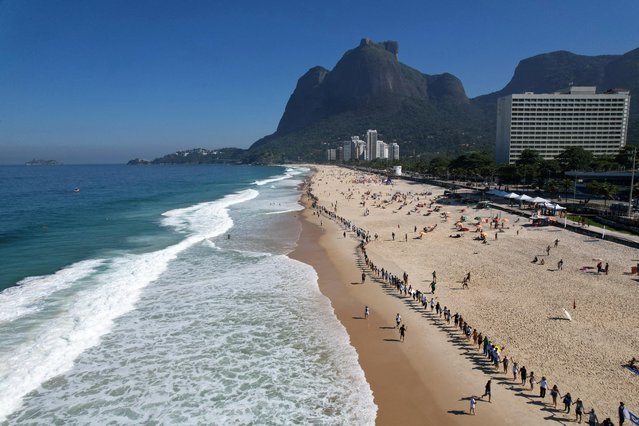 People attend a symbolic ritual named “Aquele Abraco” (That Hug), which represents a hug to the ocean, marking the World Oceans Day, at Sao Conrado beach in Rio de Janeiro, Brazil on June 8, 2023. (Photo by Pilar Olivares/Reuters)