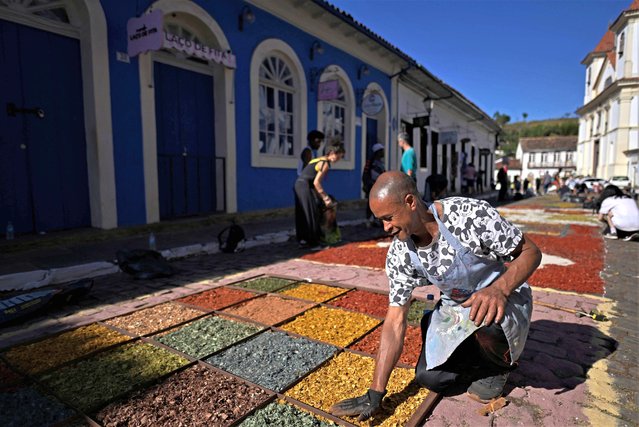 A catholic devotee participates on the elaboration of a sawdust and sand carpet before the Corpus Christi procession in Marina, Minas Gerais state, Brazil on June 8, 2023. (Photo by Douglas Magno/AFP Photo)