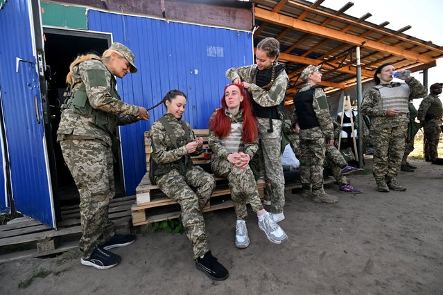 Female Ukrainian cadets, wearing new military uniforms designed specially for women, have their hair braided as they take part in a training during the “Uniform matters” event organised to present the outfit and test it under military training conditions, on the outskirts of Kyiv on July 12, 2023. (Photo by Sergei Supinsky/AFP Photo)