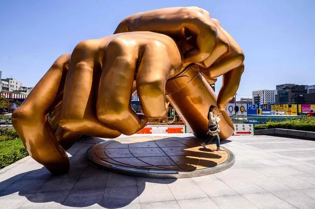 In this picture taken on June 1, 2022, a woman walks under a bronze sculpture by artist Hwang Man-seok, modeled after the signature horse-riding hand motion of the “Gangnam Style” song by South Korean singer and producer PSY, in the Gangnam district of Seoul. (Photo by Anthony Wallace/AFP Photo)