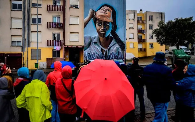 Visitors watch a mural by Portuguese artist Nomen during a guided visit to Quinta do Mocho neighbourhood in Sacavem, outskirts of Lisbon, on November 11, 2019. The image of a black woman removing her white-woman mask is one of the hundreds of murals that cover the buildings of the underprivileged district of Quinta de Mocho in Lisbon, that has been transformed by street art. (Photo by Patricia De Melo Moreira/AFP Photo)