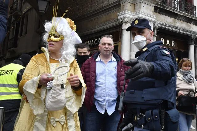 A policeman wearing a sanitary masks gestures next to a reveler in Venice, Sunday, February 23, 2020. Italian authorities have announced they are shutting down Venice's famed carnival events in a bid to stop the spread of the novel virus, as numbers of infected persons in the country have soared to at least 133, the largest amount of cases outside Asia. (Photo by Luigi Costantini/AP Photo)