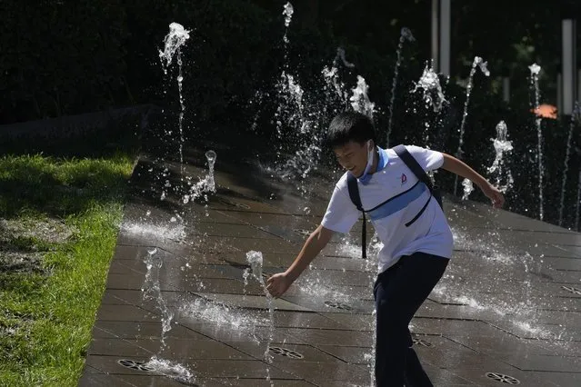 A teenager plays with a water fountain during a hot day, Thursday, July 14, 2022, in Beijing. (Photo by Ng Han Guan/AP Photo)