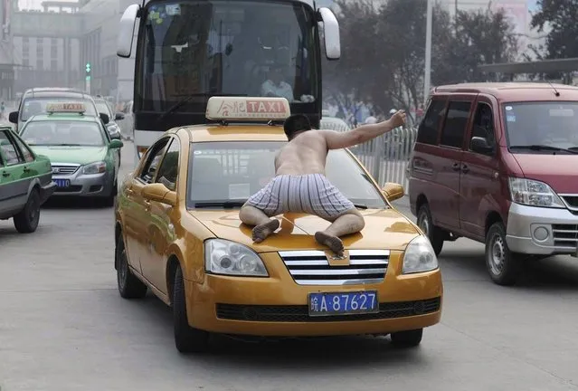 A topless man smashes the windshield of a taxi in the middle of a street in Hefei, Anhui province July 17, 2012. The man ran onto a busy street on Tuesday morning wearing only a pair of shorts, climbing onto cars and smashing windows with his bare fists. He was taken away to the hospital by policeman and doctors after smashing nearly 20 vehicles in half an hour. Police said there was no identification with the man, and he would go through psychiatric examination to determine whether he was mentally ill, local media reported. Picture taken July 17, 2012. (Photo by Stringer/Reuters)
