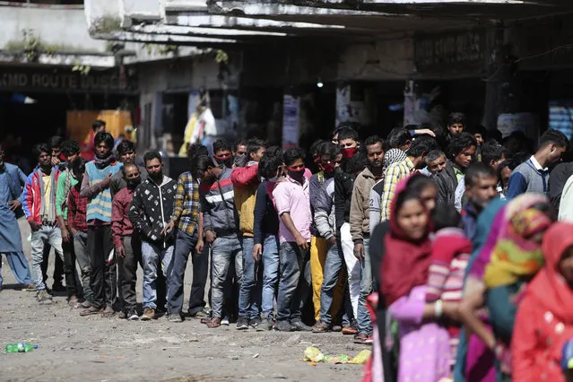 Indian passengers who got stranded at a bus terminal line up for free food being distributed by shop keepers during a day long lockdown amid growing concerns of coronavirus in Jammu, India, Sunday, March 22, 2020. (Photo by Channi Anand/AP Photo)