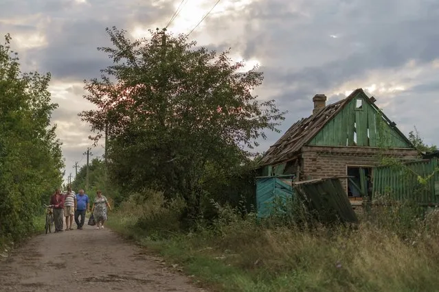 Residents walk down a road Tuesday, August 16, 2022, past a damaged home from a morning rocket attack in Kramatorsk, eastern Ukraine as Russian shelling continued to hit towns and villages in Donetsk province, regional officials said. (Photo by David Goldman/AP Photo)