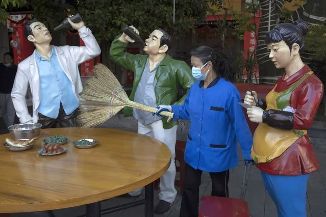 A cleaner wearing a mask to help stop the spread the coronavirus sweeps replicas of food and statues depicting normal life along a retail street in Wuhan, central China's Hubei province, Thursday, April 9, 2020. Released from their apartments after a 2 1/2-month quarantine, residents of the city where the coronavirus pandemic began are cautiously returning to shopping and strolling in the street but say they still go out little and keep children home while they wait for schools to reopen. (Photo by Ng Han Guan/AP Photo)