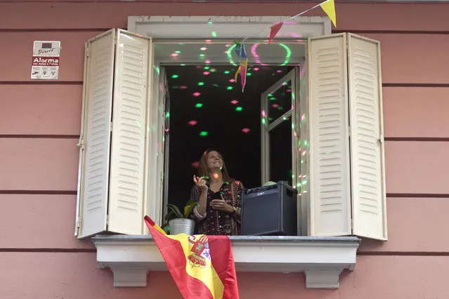 A woman stands by her open window while playing amplified music and with disco lights, as the lockdown to combat the spread of coronavirus continues in Madrid, Spain, Monday, April 13, 2020. Many people are inventive and inspirational as they combat the social effects of self isolation. (Photo by Paul White/AP Photo)