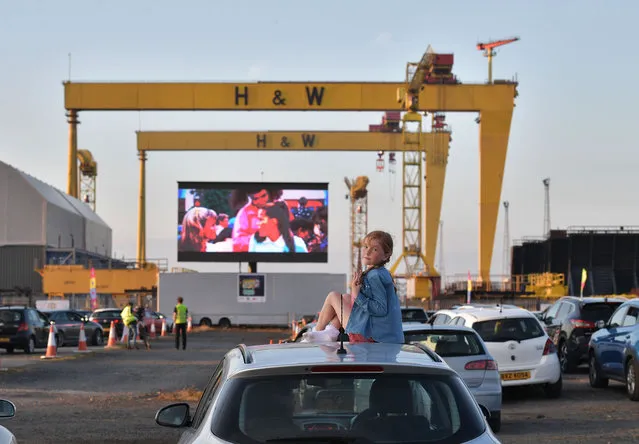 Bridget Nolan watches Grease on the big screen from the roof of her mothers car in the Titanic Quarter beneath the famous Harland and Wolff cranes on June 13, 2020 in Belfast, Northern Ireland. The drive-in cinema is the first of its kind taking place in the UK as some of the restrictions surrounding the Covid-19 pandemic are relaxed. Drive-In Cinema Belfast who organised the event will donate all the profits towards Covid-19 research at Queens University, Belfast. (Photo by Charles McQuillan/Getty Images)