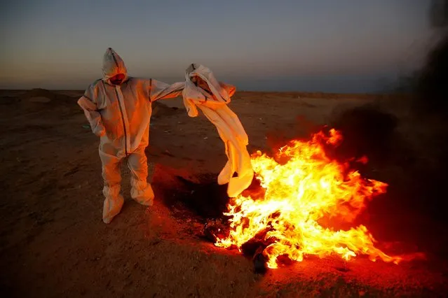 A member of the Popular Mobilization Forces (PMF), who volunteered to work in a cemetery, wears a protective suit, as he burns clothes they used for burial, near the new Wadi Al-Salam cemetery, which is dedicated to those who died of the coronavirus disease (COVID-19), on the outskirts of the holy city of Najaf, Iraq on May 25, 2020. (Photo by Alaa al-Marjani/Reuters)