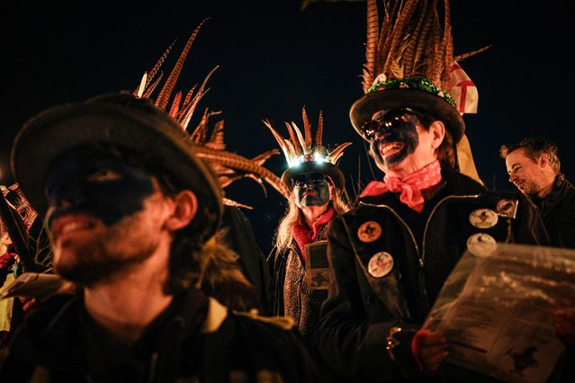Members of the Hook Eagle Morris Men gather in the orchard during the annual Wassail night in Hartley Wintney, west of London on January 12, 2024. The event, held near to twelfth night, celebrates both the passing of Christmas and the future good health of the fruit trees. Traditionally the custom involved the local farm workers visiting the orchard after dark with shotguns, horns, food and a large pail of cider. They would make a loud noise to raise the Sleeping Tree Spirit and to scare off demons. Cider would be poured over the roots and pieces of toast placed in the branches as a gift to the spirit of the tree. The wassail song is sung as a blessing or charm to bring fruitfulness or even in admonishment not to fail in the upcoming year. (Photo by Adrian Dennis/AFP Photo)