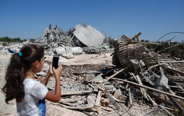 A Palestinian girl photographs the rubble of a house, that was demolished by Israeli army bulldozers, in the village of Qalandia, next to Israel's controversial separation barrier, between the Israeli occupied West Bank town of Ramallah and East Jerusalem on July 26, 2016. Israeli authorities demolished a dozen Palestinian homes in Qalandia, according to Palestinian sources. Witnesses added that shortly after midnight, a convoy of dozens of military vehicles and Israeli bulldozers stormed the resort, before demolishing 11 houses. (Photo by Ahmad Gharabli/AFP Photo)