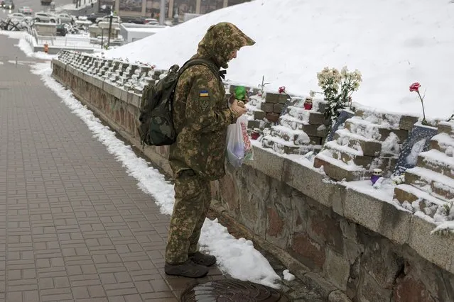 A Ukrainian serviceman lights a candle at a memorial dedicated to people who died in clashes with security forces, at the Independent Square (Maidan) in Kyiv, Ukraine, Monday, November 21, 2022. People gathered to commemorate the Maidan protest movement and the events which took place in late Feb. 2014 that led to the departure of former Ukrainian President Victor Yanukovich and the formation of a new government. (Photo by Andrew Kravchenko/AP Photo)