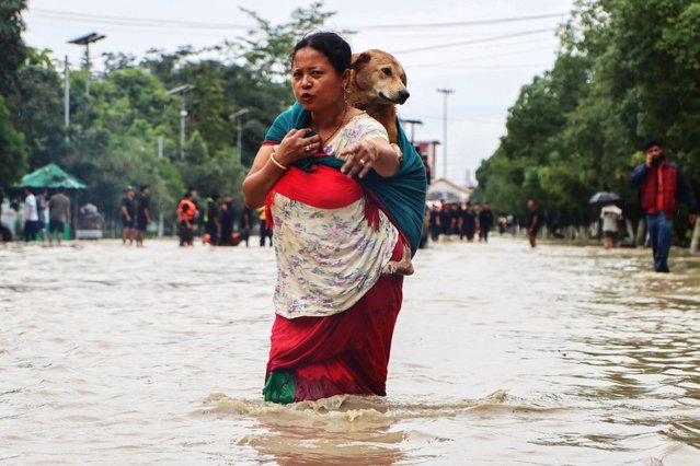 A woman carrying her pet dog wades through a flooded street following heavy rainfall in Imphal East in Indian state of Manipur on June 1, 2025. Flash floods and landslides after torrential monsoon rain over the last two days killed at least 30 people in India's northeast, officials said June 1. (Photo by AFP Photo/Stringer)