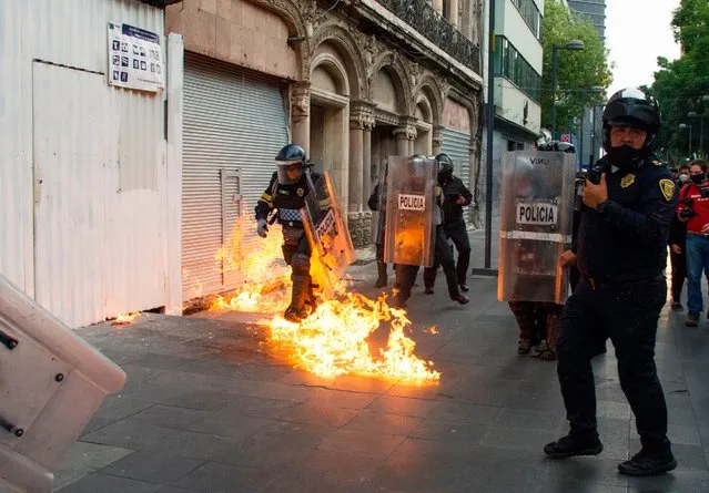 A policeman walks over a burning molotov cocktail thrown by demonstrators in Mexico City on September 26, 2020, during a march for the sixth anniversary of the disappearance of 43 students of the Ayotzinapa Teacher Training College. The students, who had commandeered five buses to travel to a protest, were stopped by municipal police in the city of Iguala, Guerrero. Prosecutors initially said the officers delivered the 43 teacher trainees to drug cartel hitmen, who killed them, incinerated their bodies and dumped the remains in a river. However, independent experts from the Inter-American Commission on Human Rights have rejected the government's conclusion. (Photo by Claudio Cruz/AFP Photo)