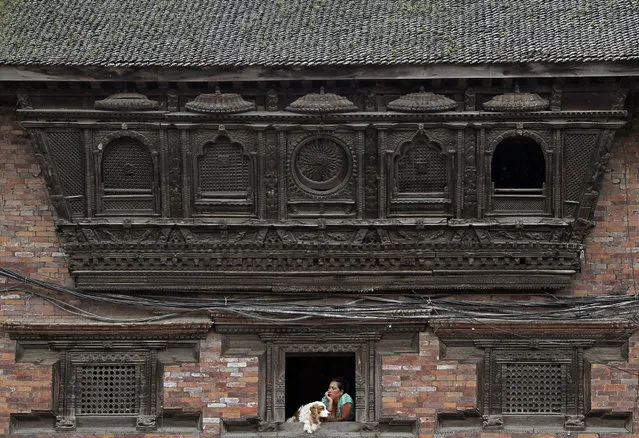 A Nepalese woman sits with her dog and watches outside from an artistically crafted wooden window in Bhaktapur, Nepal, Monday, September 12, 2016. Bhaktapur, also known as the city of devotees, is an ancient city popular for its traditional architectural buildings, temples and unique festivals. (Photo by Niranjan Shrestha/AP Photo)