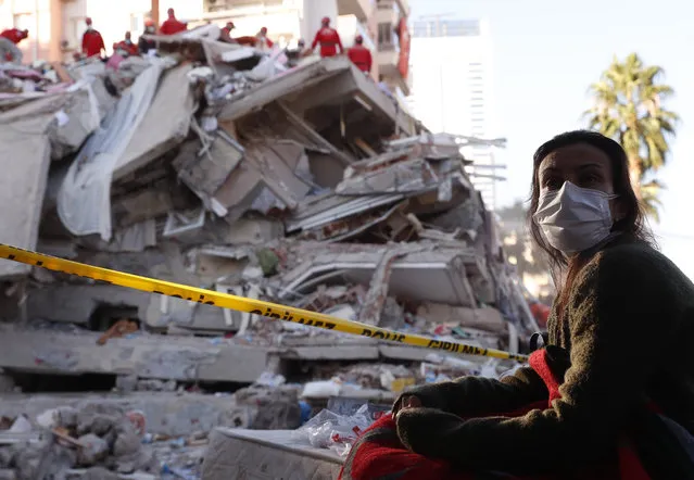 A local resident, staying outdoors for fear of aftershocks, watches as members of rescue services search for survivors in the debris of a collapsed building in Izmir, Turkey, Saturday, October 31, 2020. Rescue teams on Saturday ploughed through concrete blocs and debris of eight collapsed buildings in Turkey's third largest city in search of survivors of a powerful earthquake that struck Turkey's Aegean coast and north of the Greek island of Samos, killing dozens Hundreds of others were injured. (Photo by Darko Bandic/AP Photo)