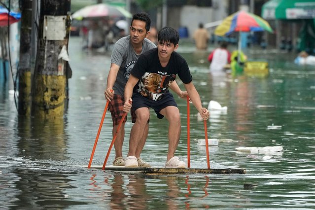 Residents use poles as they ride an improvised float along a flooded road as Typhoon Co-may intensified seasonal monsoon rains at Malabon city, Philippines on Friday, July 25, 2025. (Photo by Aaron Favila/AP Photo)