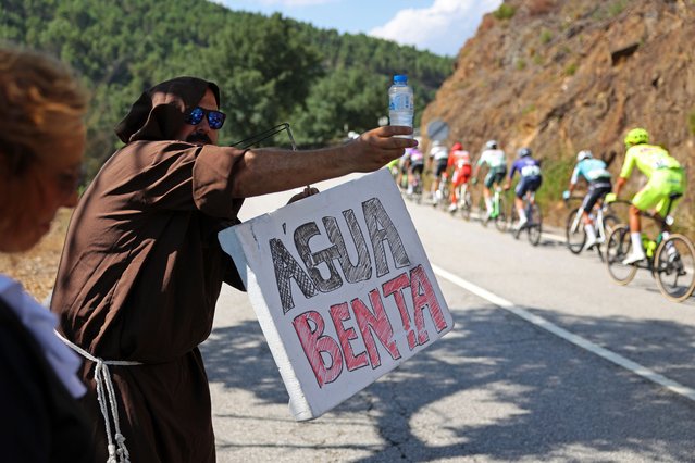 A fan dressed as a priest holds a banner with the words "Holy Water" as he offers water to a rider during the 6th stage of the 85rd Portugal Cycling Tour over 169,1 Km, between Bragança and Boticas, Portugal, 31 July 2024. *Photo by Nuno Veiga/LUSA)