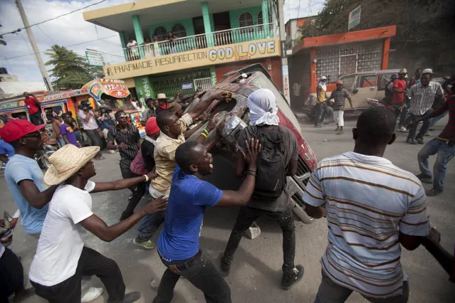 Demonstrators flip a car to block off a street during a protest demanding the resignation of President Michel Martelly in Port-au-Prince, Haiti, Sunday, January 11, 2015. At the same time, Martelly and opposition officials were locked again in negotiations at a hotel, trying to forge a last-minute deal to resolve a standoff that's stalling elections. Martelly will rule by decree if they don't resolve the political crisis by the end of Monday. (Photo by Dieu Nalio Chery/AP Photo)
